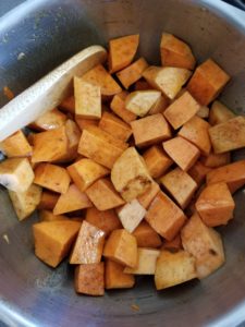 Sweet potatoes in mixing bowl with olive oil and pumpkin spice.