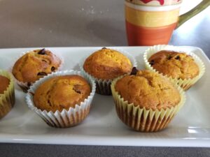 Pumpkin chocolate chip muffins on a plate with a coffee cup in the background.