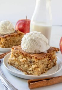 Apple blondies on plates with scoop of ice cream on top. Apple and jar of milk in the background.